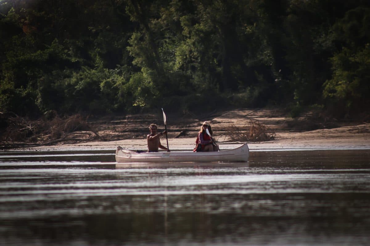 Dos personas remando en canoa por un río rodeado de monte